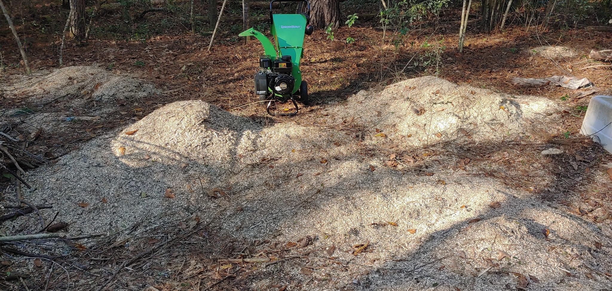 Several large mounds of wood chips made by a GardenBeaut chipper in a wooded lot